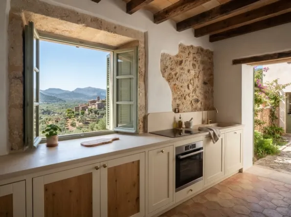 Küchenfenster mit Blick auf terrassierte Olivenhaine, ein Steindorf auf einem Hügel und Berge, über einer hellen Stein-Arbeitsplatte