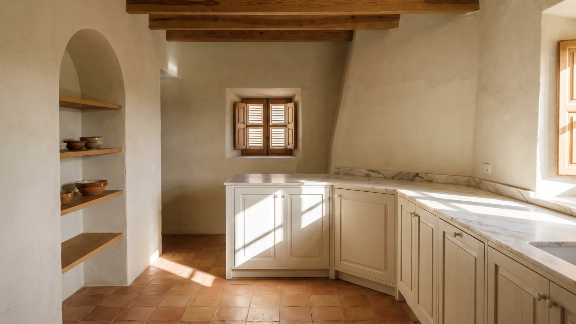 Warmweiße Küchenmöbel entlang einer schrägen Wand unter einer Marmor-Arbeitsplatte, Eichenregale in einer Bogennische, ein Terrakottaboden