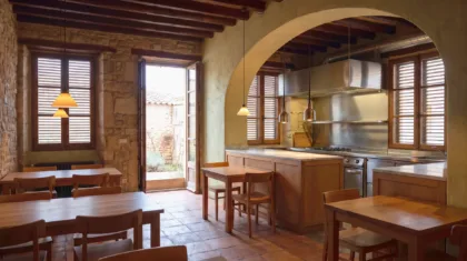 Restaurant-Speisesaal mit Holztischen und einem Steinbogen zu einer Stahlküche, geschlossene Fensterläden und brennende Pendelleuchten