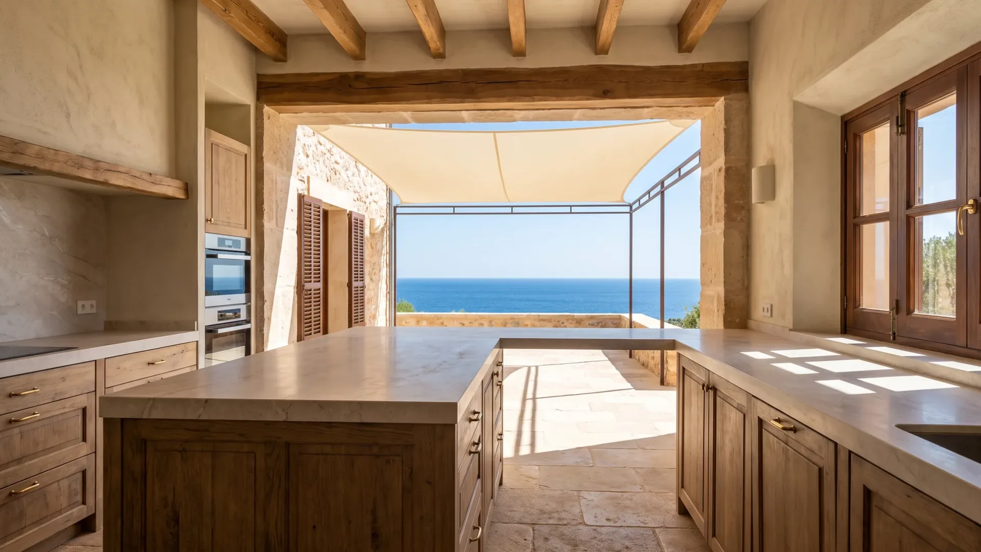 Eichenküche mit steinbedeckter Kücheninsel gegenüber einer Öffnung zu einer Terrasse mit Meerblick unter Sonnensegel, Steinwände und Balken