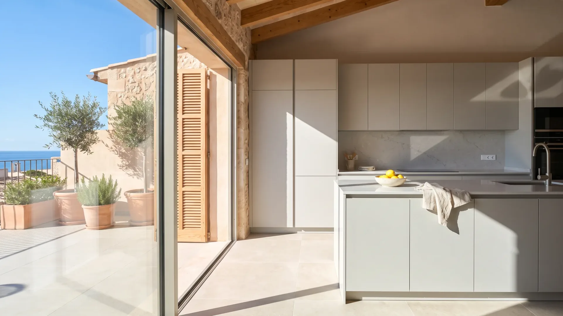 Neue Wohnungsküche in Hellgrau mit Arbeitsplatte und Küchenrückwand aus Quarzstein, Glastüren zu einer Terrasse mit Olivenbäumen in Kübeln