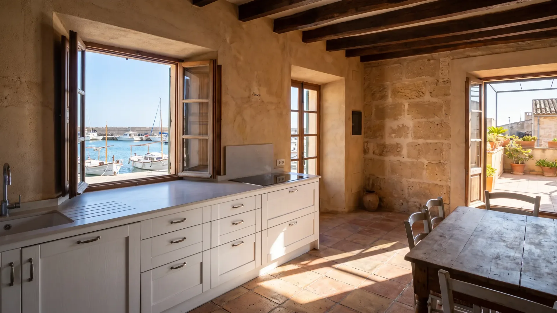 Harbour-side kitchen with white cabinetry and a pale worktop, windows onto moored boats and a timber table by a door