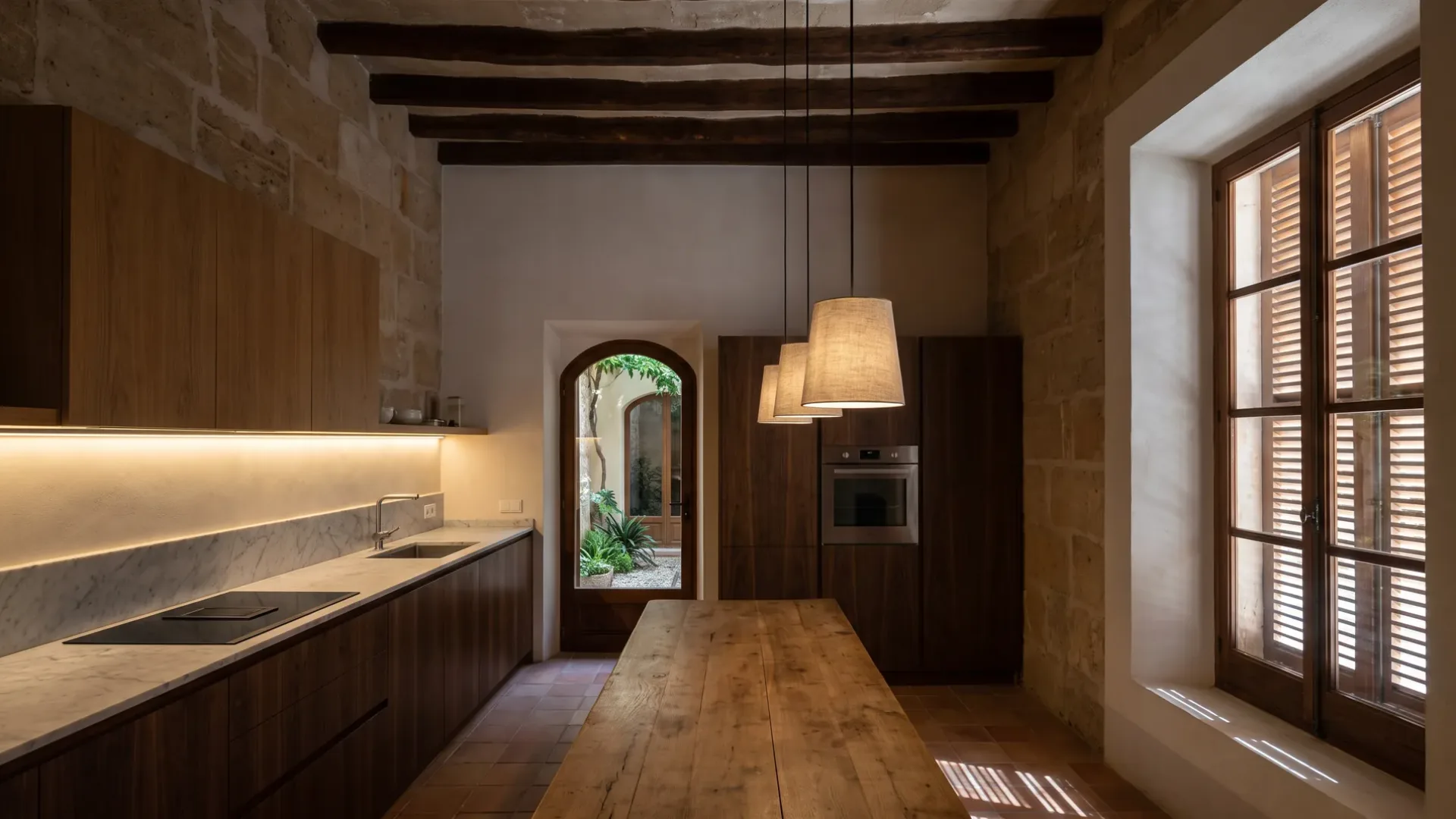 Dim walnut kitchen lit by linen pendants over an oak table and a light strip over marble, the shutters nearly closed