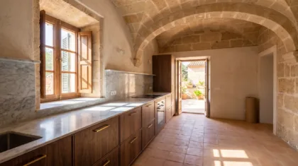 Vaulted kitchen with walnut cabinetry and a veined marble worktop and splashback, sunlight across a terracotta floor
