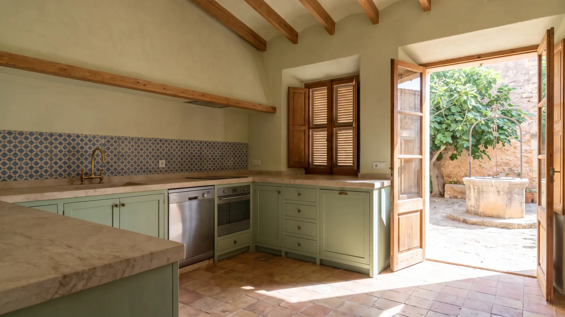 Finca-Küche in Salbeigrün mit Kalkstein-Arbeitsplatte und Rückwand aus blauen und cremefarbenen Fliesen, eine Tür zum Brunnen im Innenhof