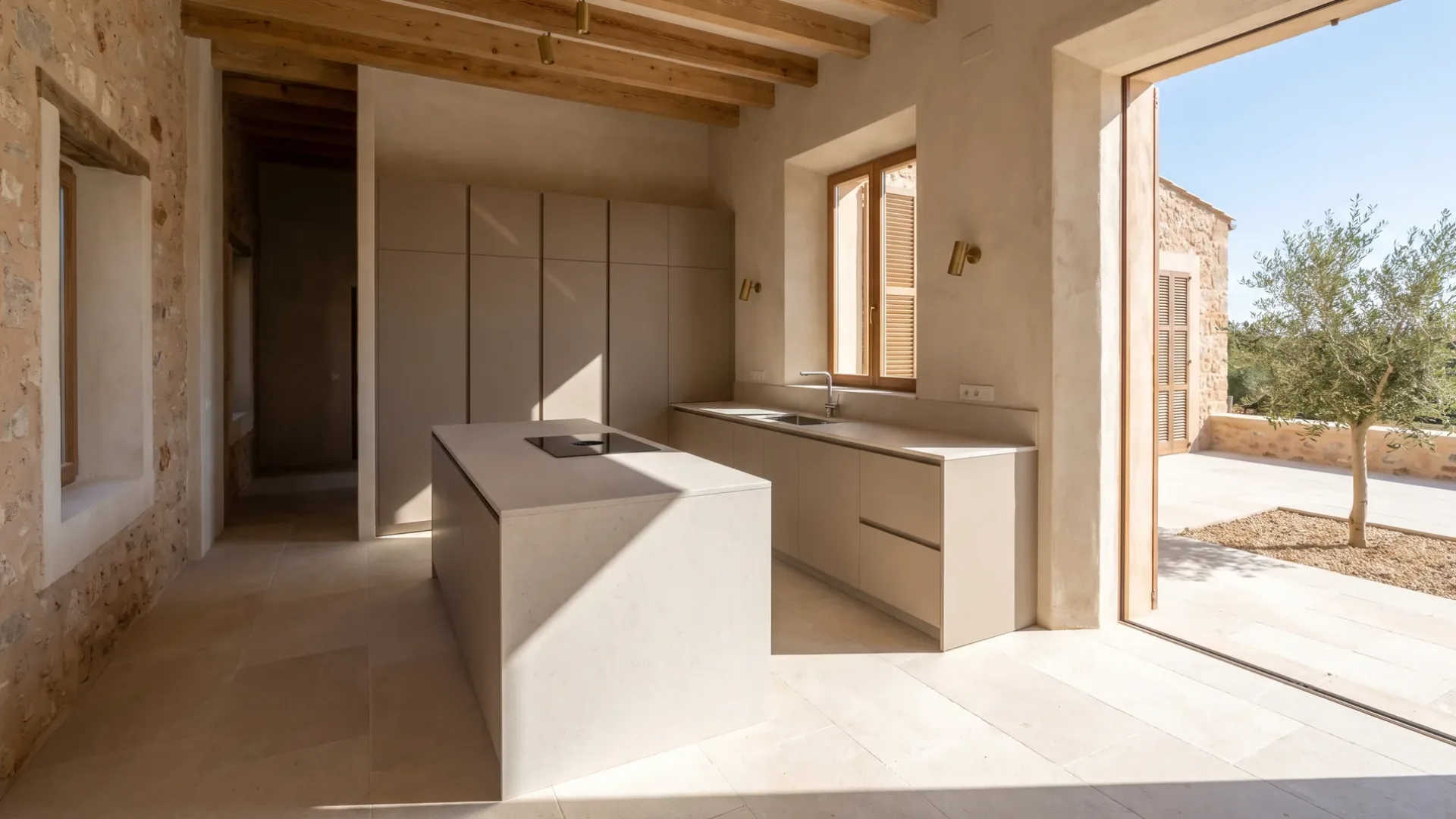 Neue Villa-Küche in mattem Taupegrau mit heller Kücheninsel und bündigem Kochfeld, Verglasung zu einer Terrasse und einem Olivenbaum