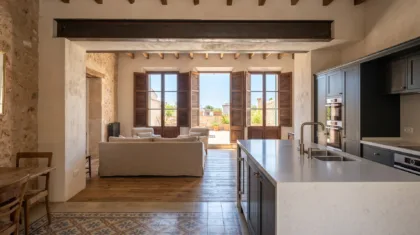 Offene Küche mit dunklen Schränken und einer weißen Steininsel gegenüber einem Wohnzimmer mit Sofa und Türen zu einer Terrasse