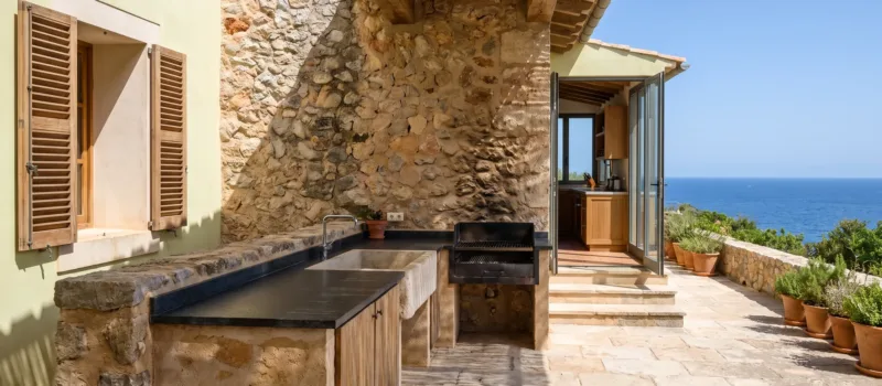 Cocina de terraza en mampostería con encimera oscura, un fregadero y una parrilla integrada junto a un muro de piedra, el mar al fondo