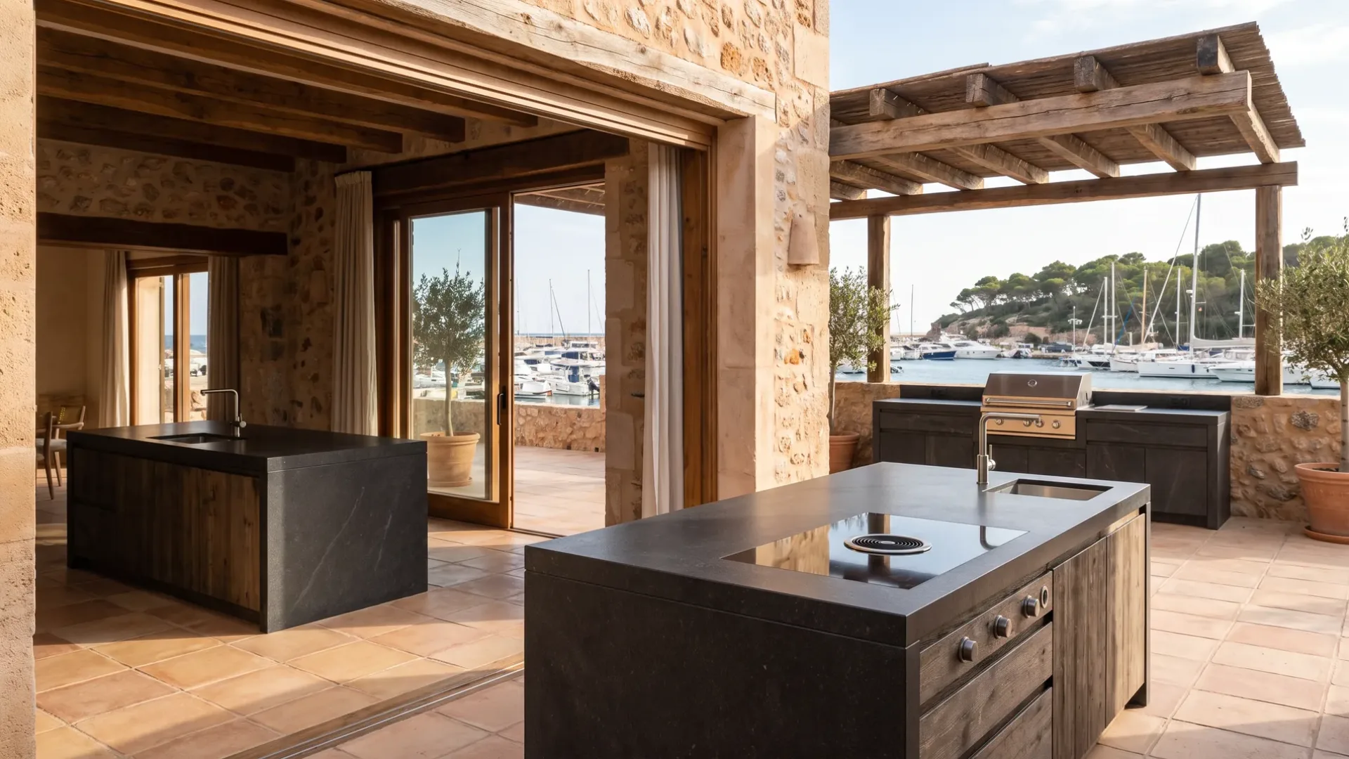 Villa-Küche mit zwei dunklen Steininseln, die sich zu einer Terrassenküche unter einer Pergola öffnen, Boote vor Anker in der Bucht